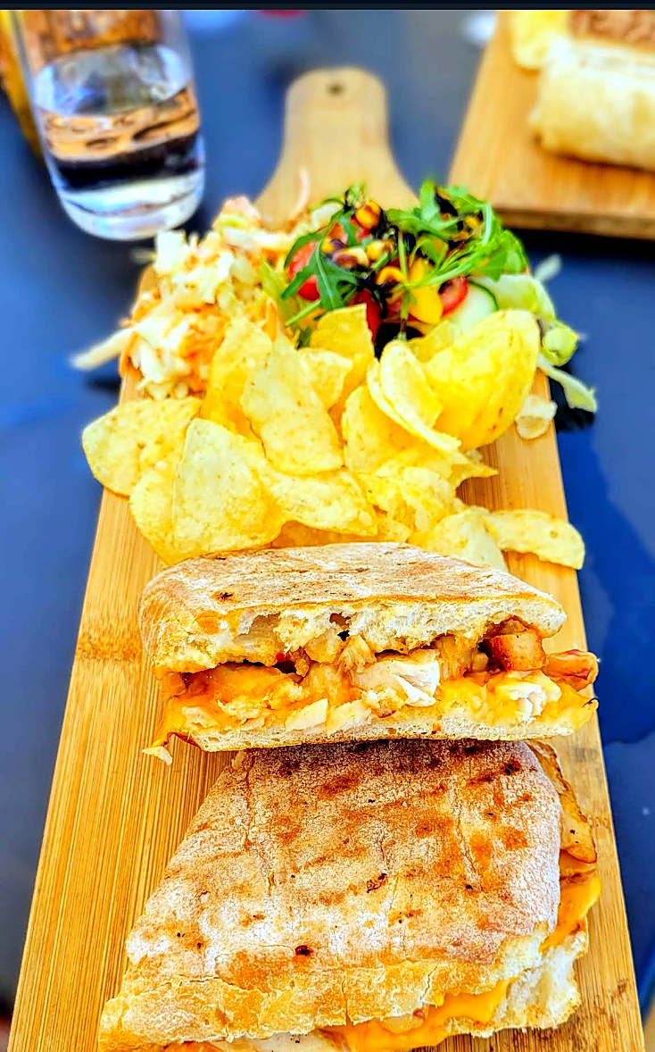 Toasted ftira with crisps and salad on a wooden serving board.