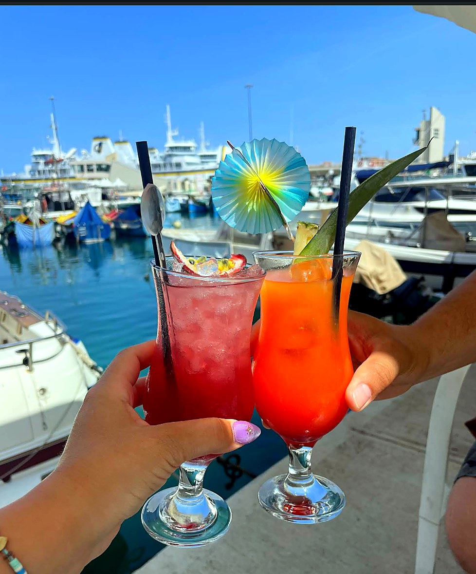Two colourful cocktails held near Mġarr harbour.