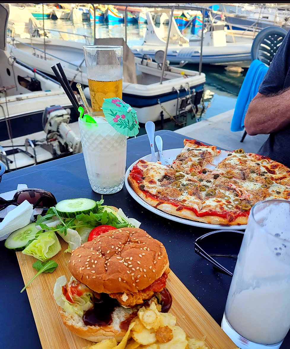Pizza, burger, drinks and salad on a harbour-side table.